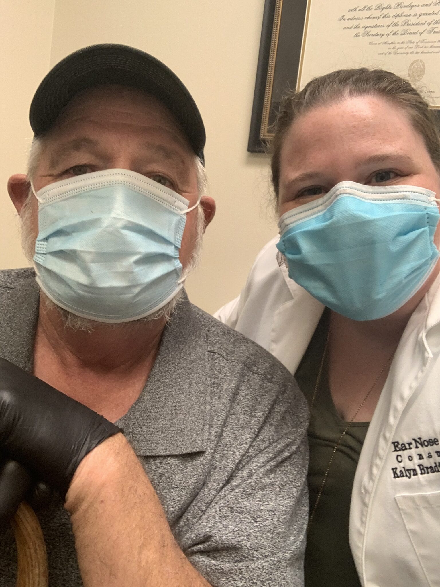 Audiologist and patient wearing face masks smiling into camera